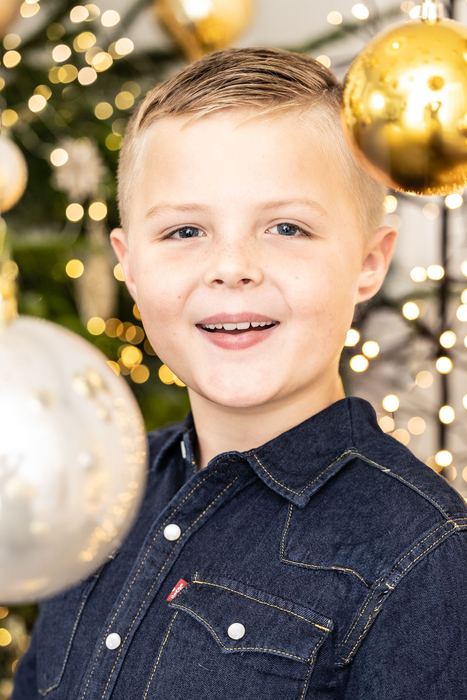 Lachender Junge vor goldenen Christbaumkugeln